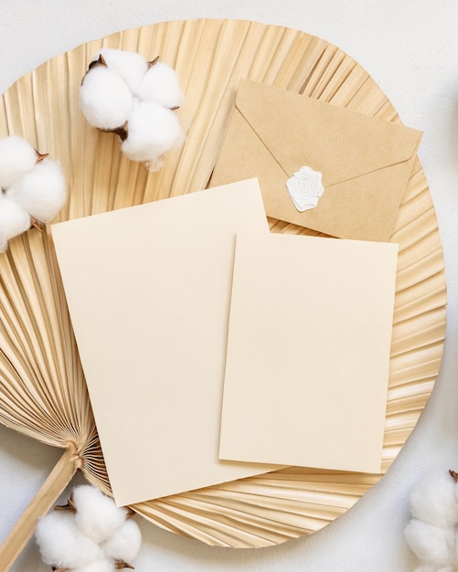 Foto tarjetas en blanco y sobre en hoja de palma seca con maqueta de boda de vista superior de flores de algodón