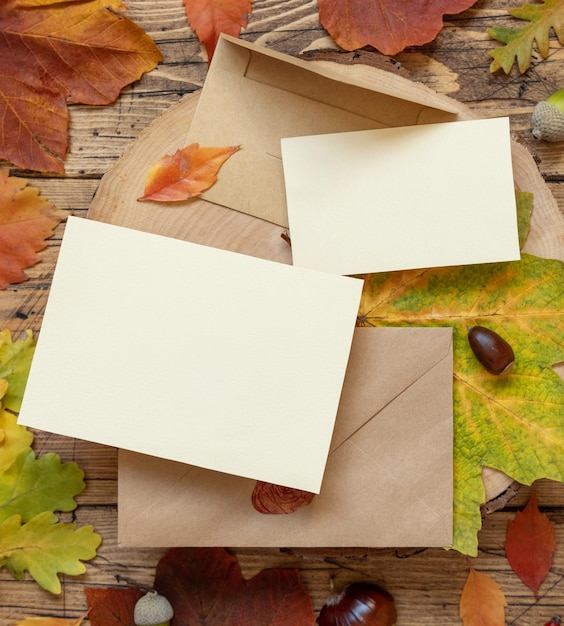 Tarjetas entre coloridas hojas de otoño y bayas en maqueta rústica de vista superior de mesa de madera