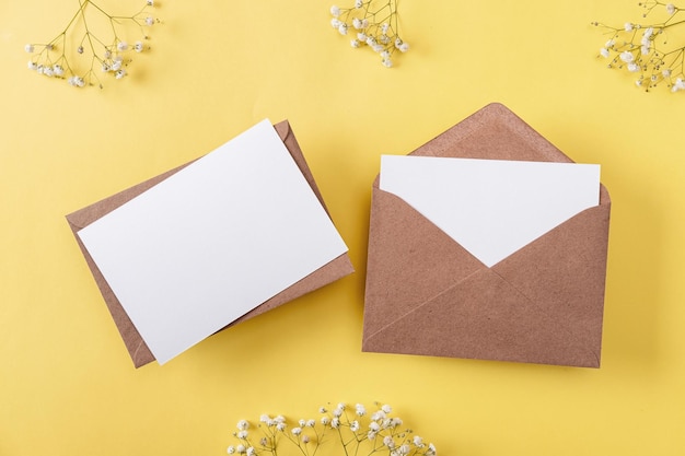 Tarjetas de felicitación en blanco y sobres con gypsophila sobre fondo amarillo Tarjetas de papel en blanco con espacio de copia de maqueta Composición mínima en el lugar de trabajo Vista superior plana