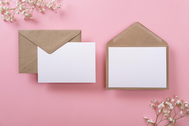 Tarjetas de felicitación en blanco y sobres con gypsophila sobre fondo rosa Tarjetas de papel en blanco con espacio de copia de maqueta Composición mínima en el lugar de trabajo Vista superior plana