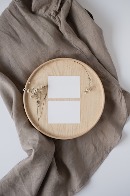 Tarjetas de hoja de papel en blanco con flores secas en ataúd de madera y manta de lino gris