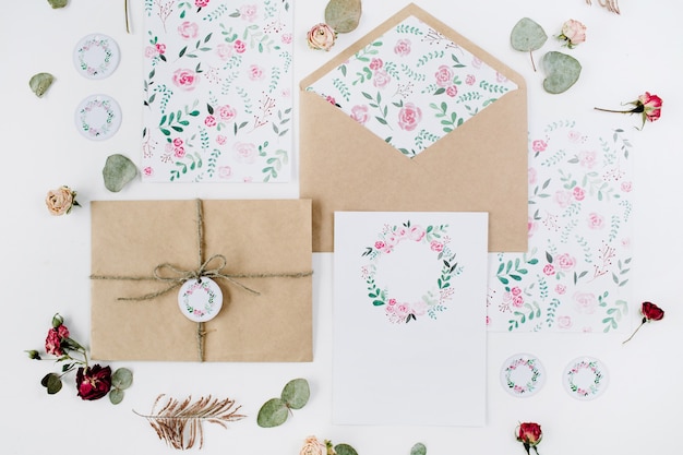 Tarjetas de invitación de boda, sobres artesanales, rosas rosadas y rojas y hojas verdes sobre blanco