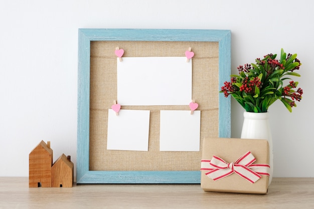 Tarjetas de papel en blanco colgando en el marco de madera vintage azul y caja de regalo en el fondo de la tabla