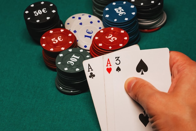 Tarjetas con un par de ases en manos de un jugador de póker en un casino en el fondo de una mesa con fichas