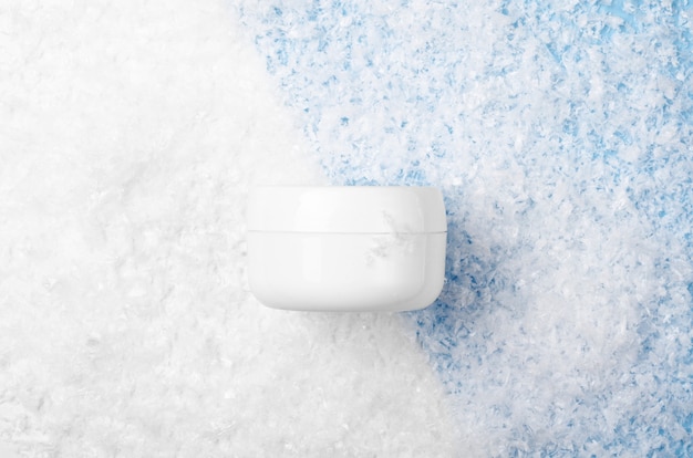 Tarro blanco con crema facial sobre un fondo blanco y azul con nieve artificial