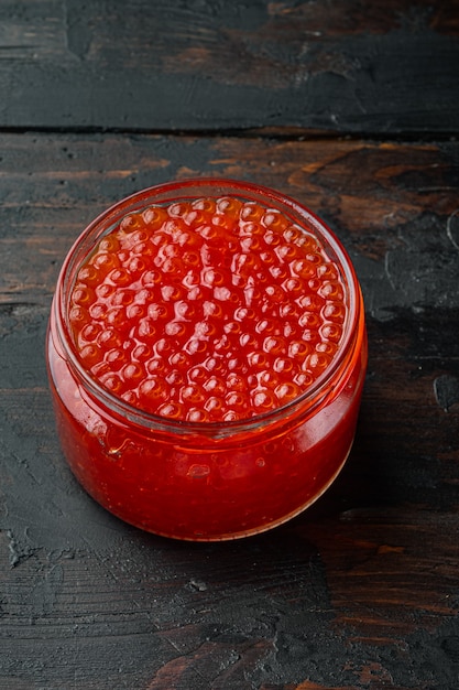 Tarro de caviar rojo, sobre fondo antiguo de mesa de madera oscura.