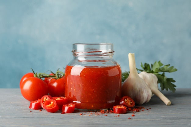 Foto tarro con chile rojo y salsa de tomate, y especias en mesa de madera