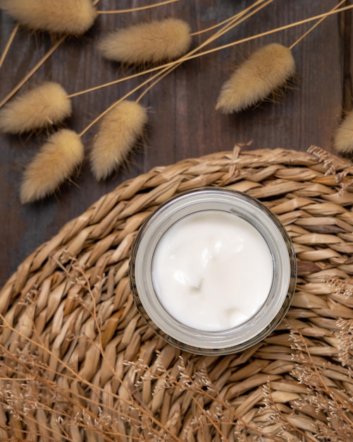 Tarro de crema abierto en un mantel de barbas cerca de la vista superior de la hierba de cola de liebre Maqueta cosmética