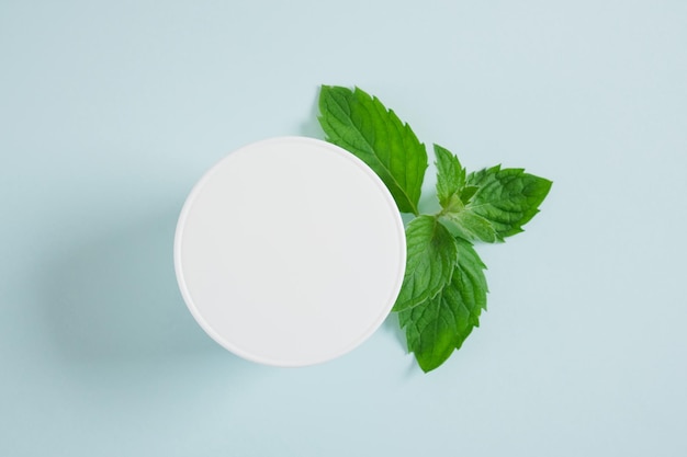 Foto tarro de crema blanca cosmética y menta fresca sobre fondo azul claro. concepto de cosmética orgánica. concepto de producto cosmético natural. producto orgánico para el cuidado de la piel