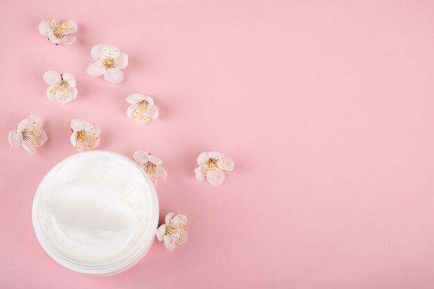 Tarro de crema y flores sobre superficie rosa