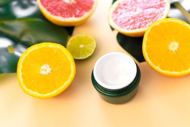 Tarro de crema hidratante facial con aceite esencial de cítricos naturales y fondo de frutas de naranja y lima