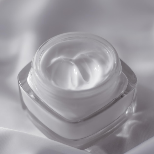 Tarro de crema hidratante facial sobre fondo de seda loción hidratante para el cuidado de la piel y cosméticos antiedad de emulsión para la marca de cuidado de la piel de belleza de lujo