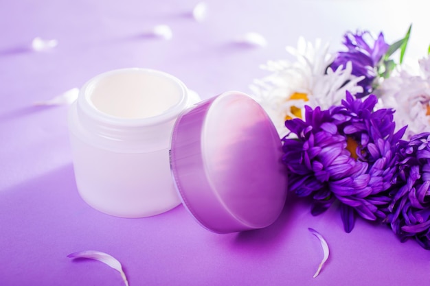 Tarro con crema rodeado de flores sobre fondo morado Cosmética orgánica Cuidado corporal