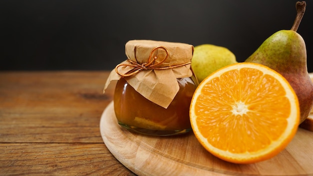 Tarro de cristal de pera casera y mermelada de naranja con frutas frescas sobre la mesa