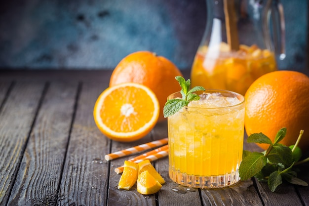 Tarro de cristal de zumo de naranja natural con hielo y frutas frescas en la mesa oscura