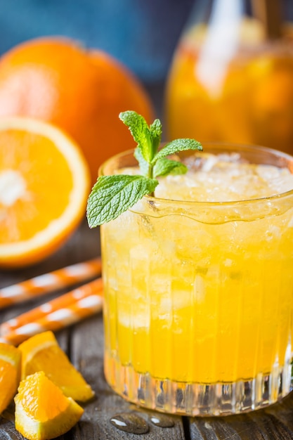 Tarro de cristal de zumo de naranja natural con hielo y frutas frescas en la mesa oscura