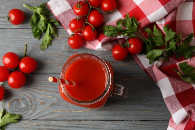 Tarro de jugo de tomate, tomates y toalla de cocina sobre fondo de madera