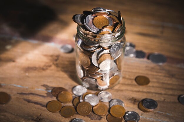 Tarro lleno de monedas en una mesa de madera