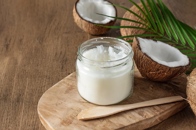 Tarro de mantequilla de coco y cocos frescos con hoja de palma sobre fondo de madera Comida vegana saludable