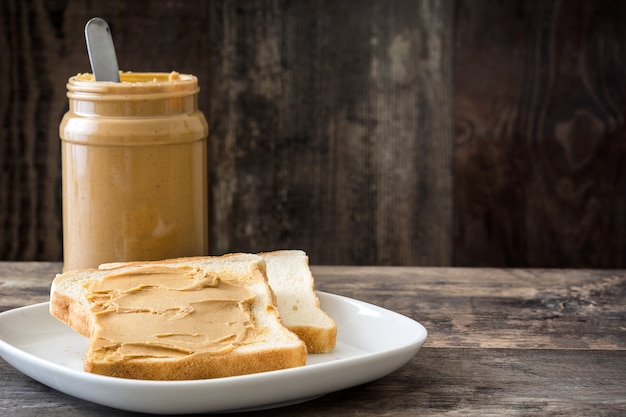 Tarro de mantequilla de maní y tostadas en mesa de madera