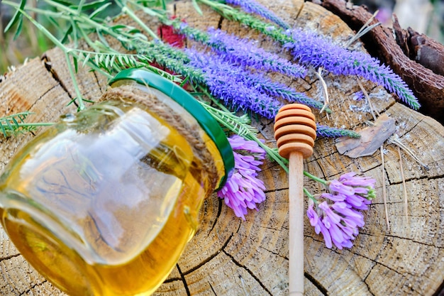 Tarro de miel y cuchara para miel en el bosque en tocón con flores de pradera