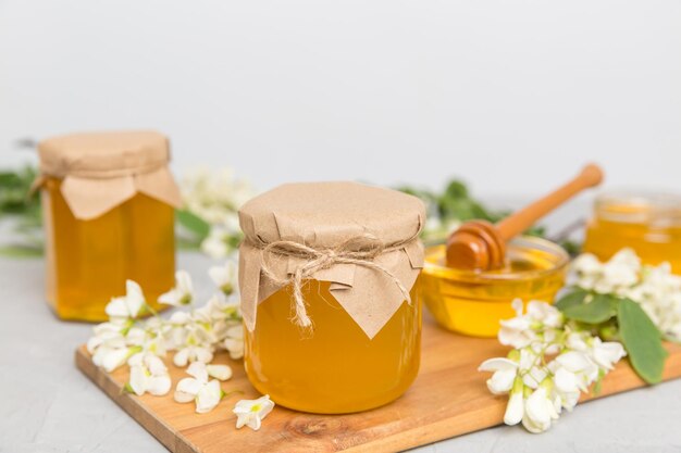 Tarro de miel dulce rodeado de flores de acacia de primavera La miel fluye de una cuchara en un tarro tarros de miel de acacia fresca clara sobre fondo de madera