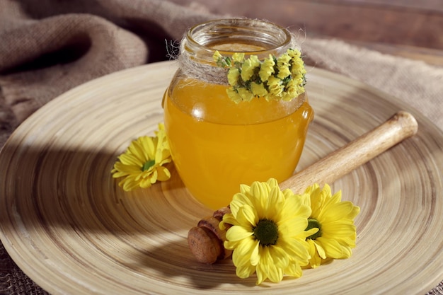 Tarro de miel con flores en bandeja de madera closeup