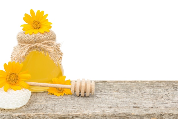 tarro de miel fresca junto a una flor y un palo de miel en una tabla de madera