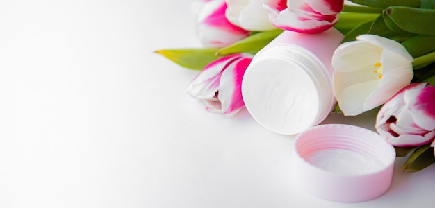 Un tarro de nata y tulipanes. Cosmetología. Protección de la piel. Mascara facial. Las flores son tulipanes. Copia espacio