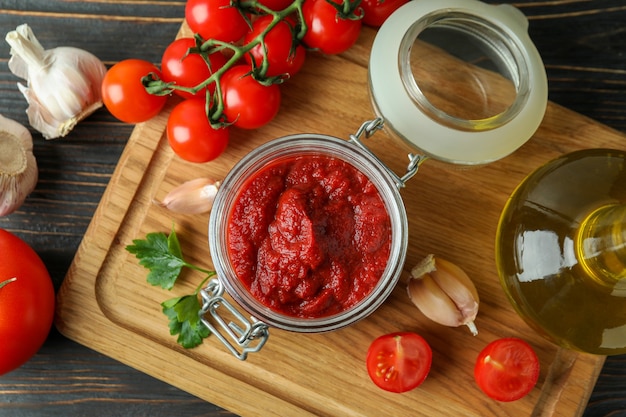 Tarro con pasta de tomate en mesa de madera con ingredientes