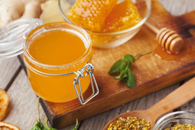 Tarro pequeño de miel natural sobre tabla de cortar de madera. Fondo dulce con varios tipos de miel