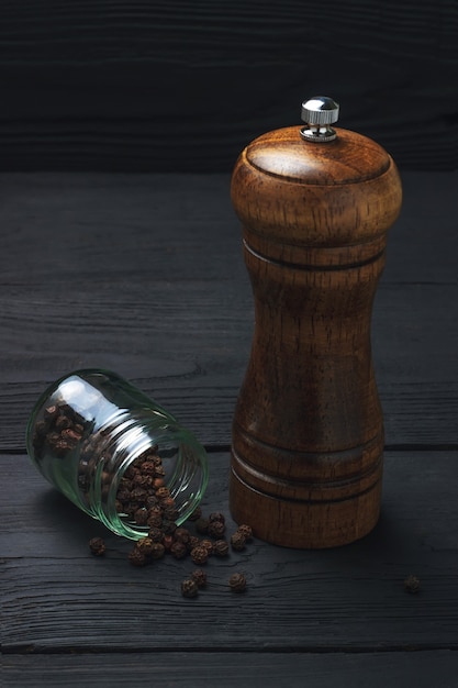 Tarro con pimienta negra y un molino sobre un fondo de madera negra