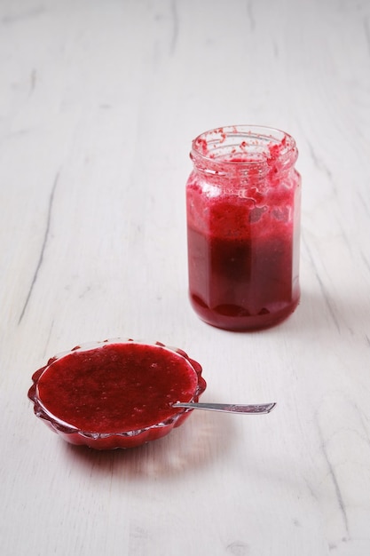 Tarro y platillo con mermelada de cereza sobre fondo blanco de madera