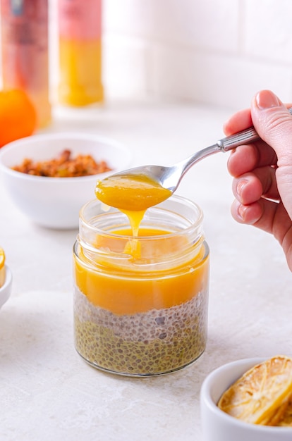 Tarro de semillas de chía y mermelada de mango. Una mujer está comiendo un postre saludable de un frasco con una cucharadita. Aperitivo agradable y apetitoso - mus tierna