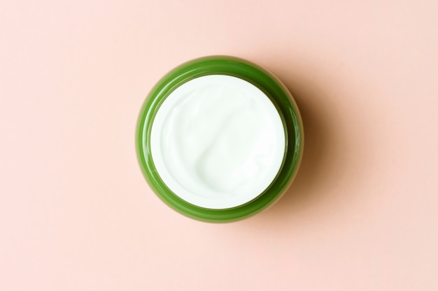 Tarro verde con crema blanca sobre un fondo rosa