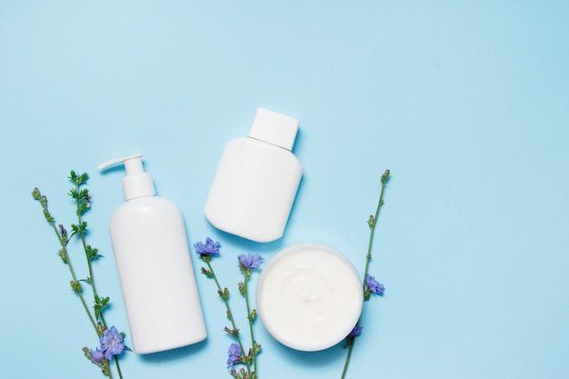 Tarros blancos de cosméticos con flores sobre un fondo azul