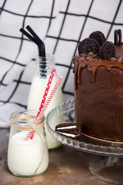 Tarros de leche con tubos brillantes junto a pastel de chocolate decorado con galletas.