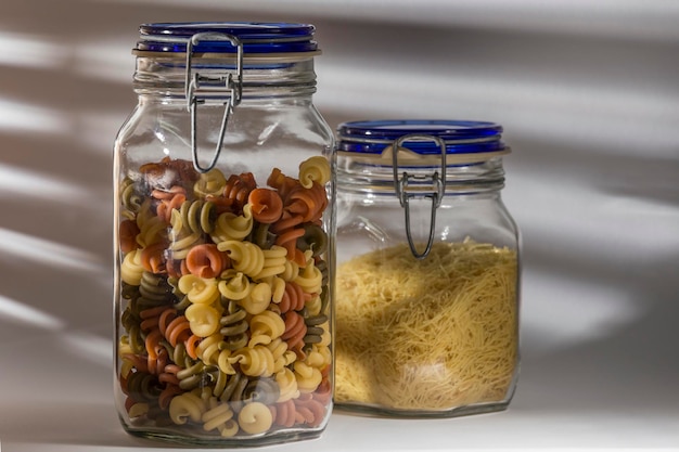 Foto tarros con pasta seca en uno fideos y en el otro espirales más altas de colores comida saludable