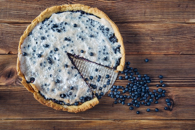 Tarta de arándanos cortada sobre una mesa rústica oscura recién salida del horno. Pila de bayas frescas cerca del postre. Vista superior.