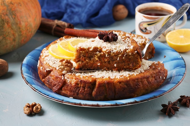 Tarta de calabaza casera con limón, canela y nueces, espolvoreada con coco, en rodajas, sobre un celeste con una taza de café