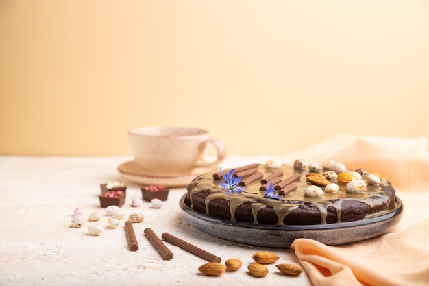 Tarta casera de brownie de chocolate con crema de caramelo y almendras con taza de café sobre un fondo blanco y naranja y textil naranja. Vista lateral, espacio de copia, enfoque selectivo.