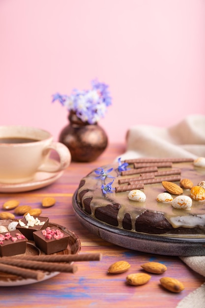 Tarta casera de brownie de chocolate con crema de caramelo y almendras con taza de café sobre un fondo de color y rosa y textil de lino. Vista lateral, espacio de copia, enfoque selectivo.