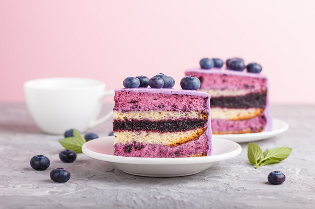 Tarta casera con crema de soufflé y mermelada de arándanos con una taza de café sobre una superficie gris y rosa. vista lateral.