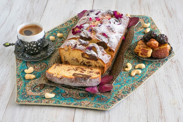 Tarta casera con dátiles y nueces, servida con café negro sobre una mesa de madera blanca