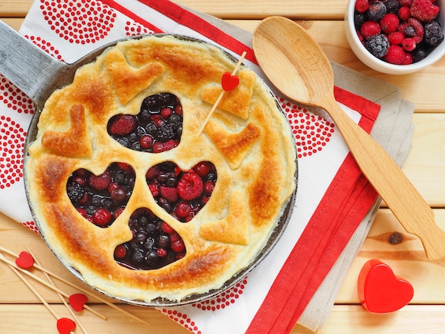 Tarta casera con frambuesas, grosellas rojas y arándanos en forma de corazón sobre superficie de madera