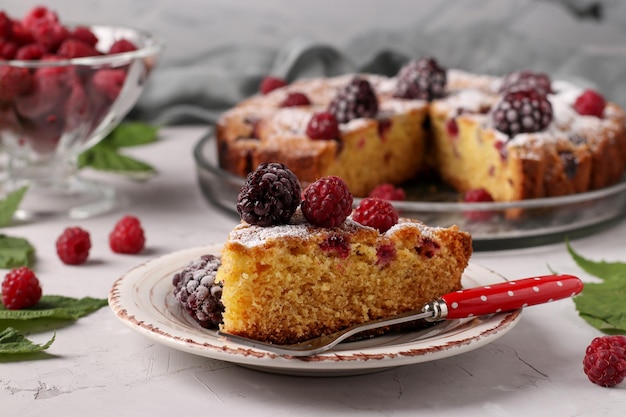 Tarta casera de moras y frambuesas con un trozo en un plato en formato horizontal de fondo gris claro