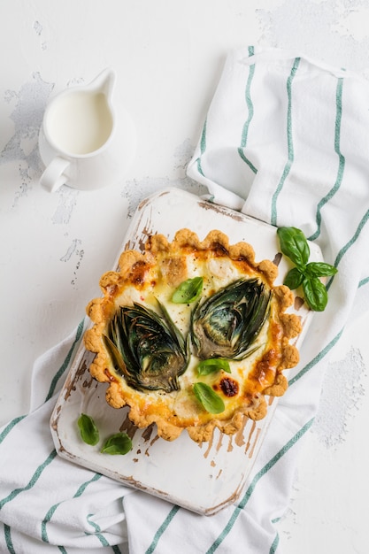 Tarta casera de quiche con alcachofa sobre fondo de madera clara.