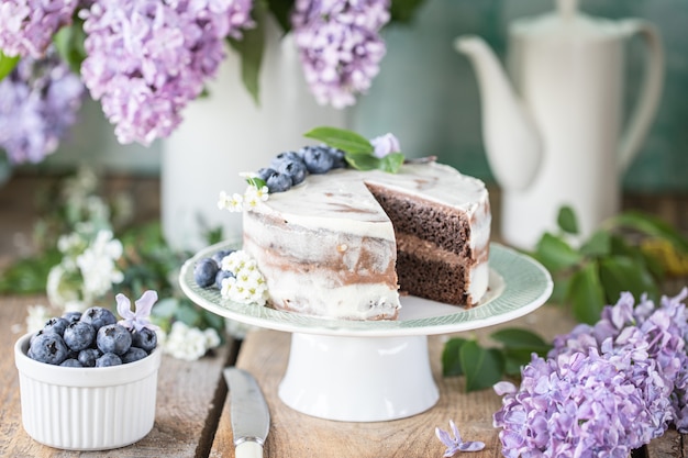 Tarta de cerezas casera con crema de mascarpone sobre un fondo claro y un ramo de flores de cerezo y lilas.