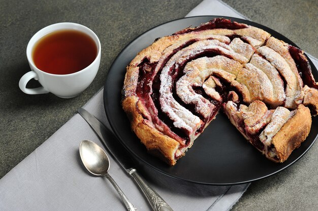 Tarta de cerezas en un plato negro y una taza de té