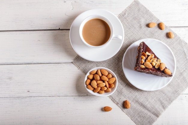 Tarta de chocolate con caramelo de maní y almendras sobre un fondo blanco de madera